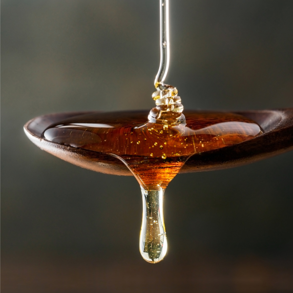 Rich, golden honey dripping from a wooden spoon, known for its natural humectant properties to lock in moisture and add shine.